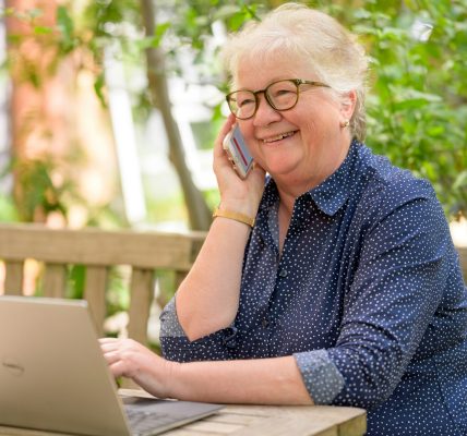 idosa de óculos quadrado com armação preta ao telefone com uma consultora MedSenior e na página da corretora https://planosdesaude.med.br/ contratando o plano MedSênior e conhecendo os 4 benefícios de ter um plano de saúde na terceira idade