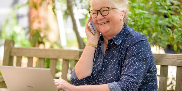 idosa de óculos quadrado com armação preta ao telefone com uma consultora MedSenior e na página da corretora https://planosdesaude.med.br/ contratando o plano MedSênior e conhecendo os 4 benefícios de ter um plano de saúde na terceira idade