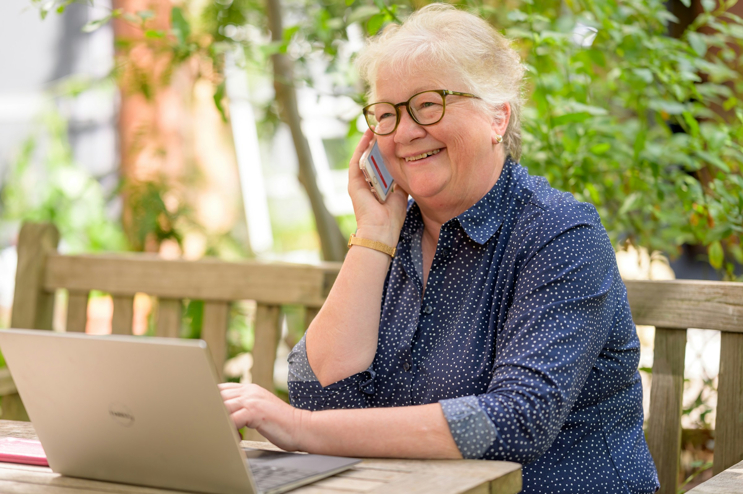 idosa de óculos quadrado com armação preta ao telefone com uma consultora MedSenior e na página da corretora https://planosdesaude.med.br/ contratando o plano MedSênior e conhecendo os 4 benefícios de ter um plano de saúde na terceira idade